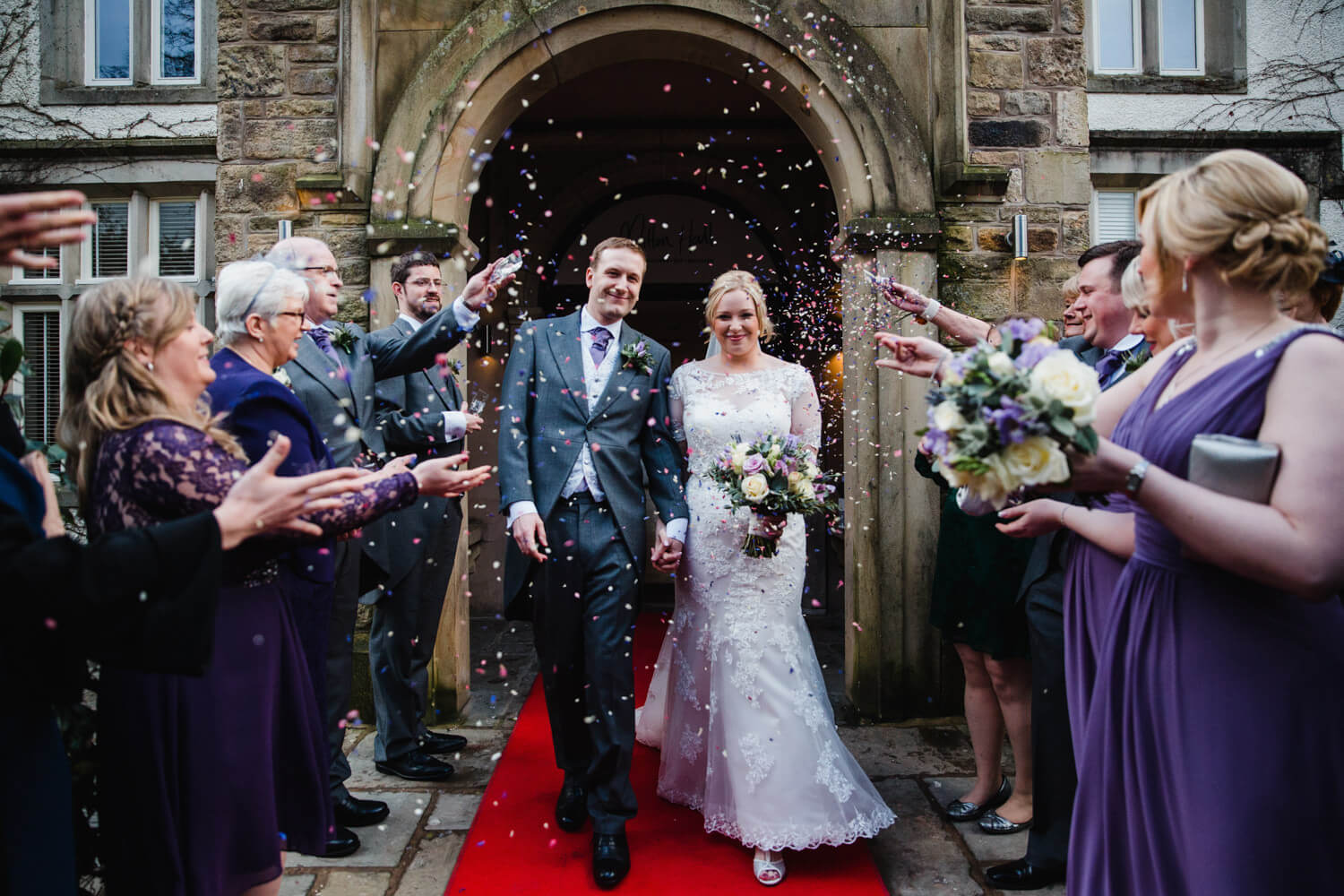 wedding party throwing confetti over newly wedded couple at Mitton Hall
