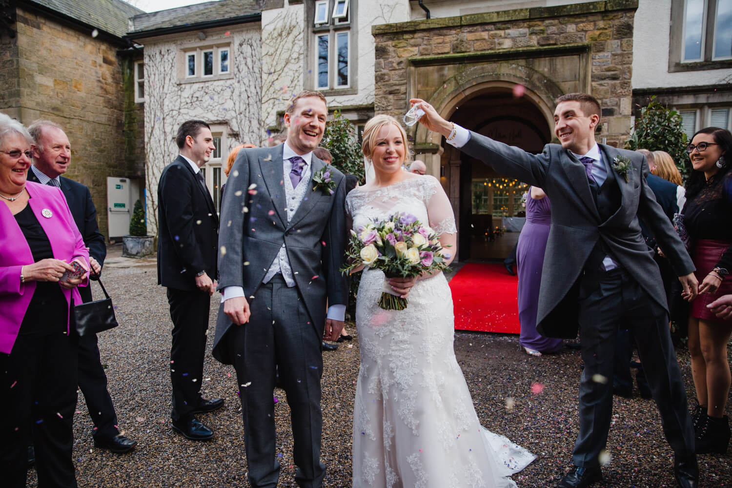 groomsman throwing confetti over newlywed couple outside Mitton Hall