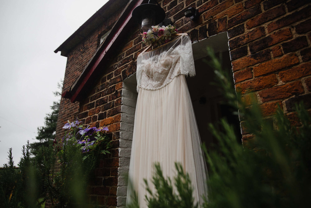 wide angle lens photograph of wedding gown hung in doorway with floral wreath head dress