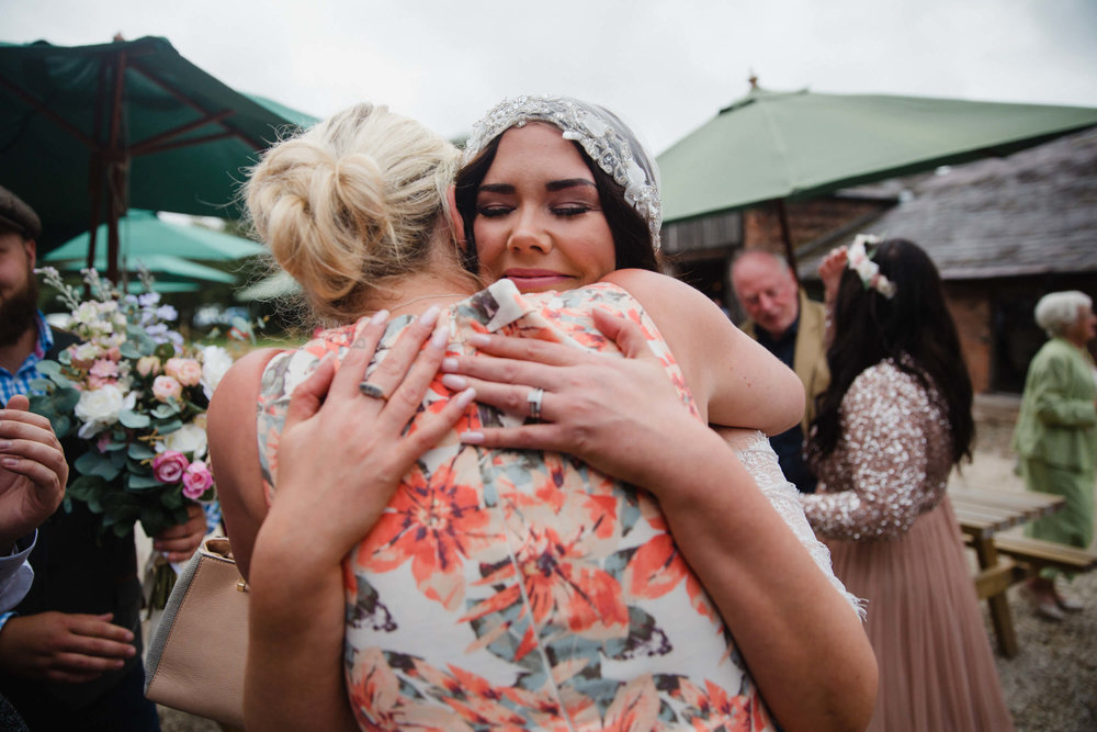 bride shares hug with wedding guest in field after wedding