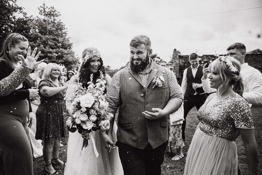 black and white monochrome photograph of newlyweds receiving confetti 