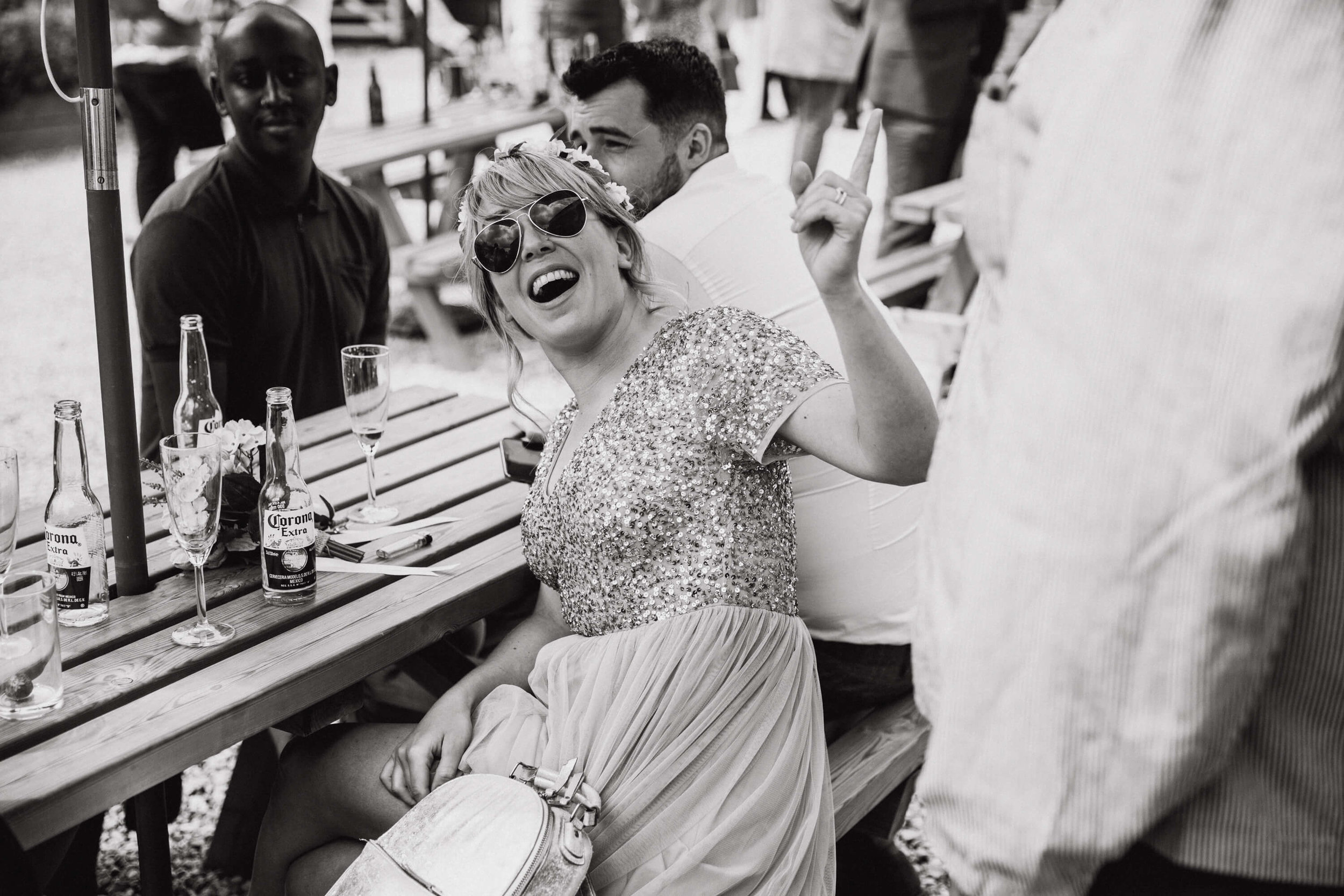 black and white monochrome photograph of bridesmaid in sunglasses laughing at guest