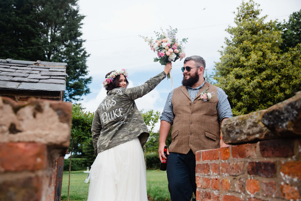 bride wearing green reserve jacket holding up bouquet in paddock