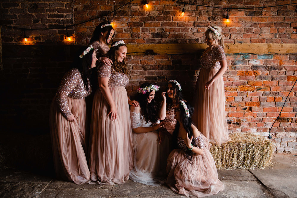 bridesmaids gather on hay bales lit up in natural light and festoon bulbs