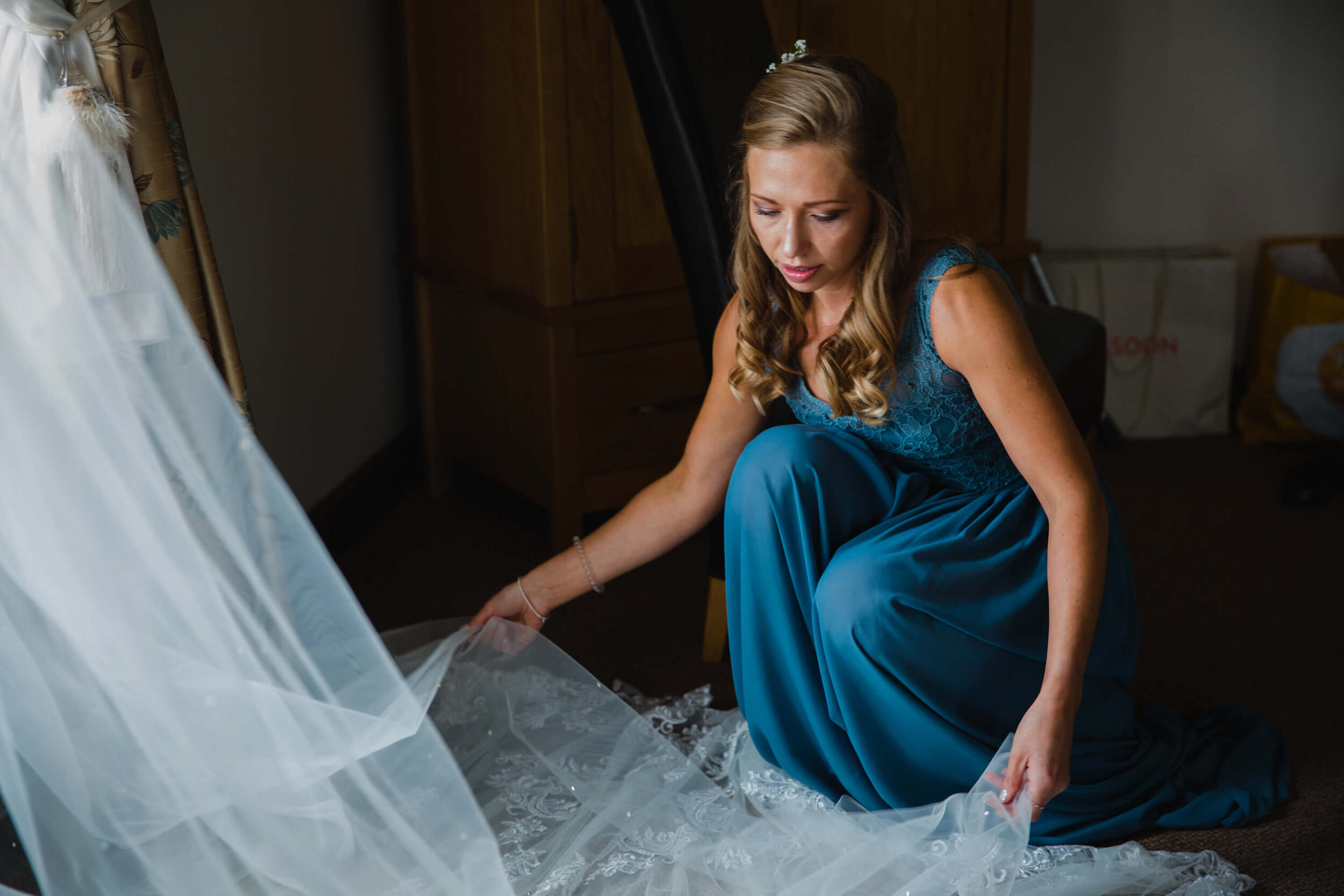 bridesmaid arranging veil of wedding dress on floor