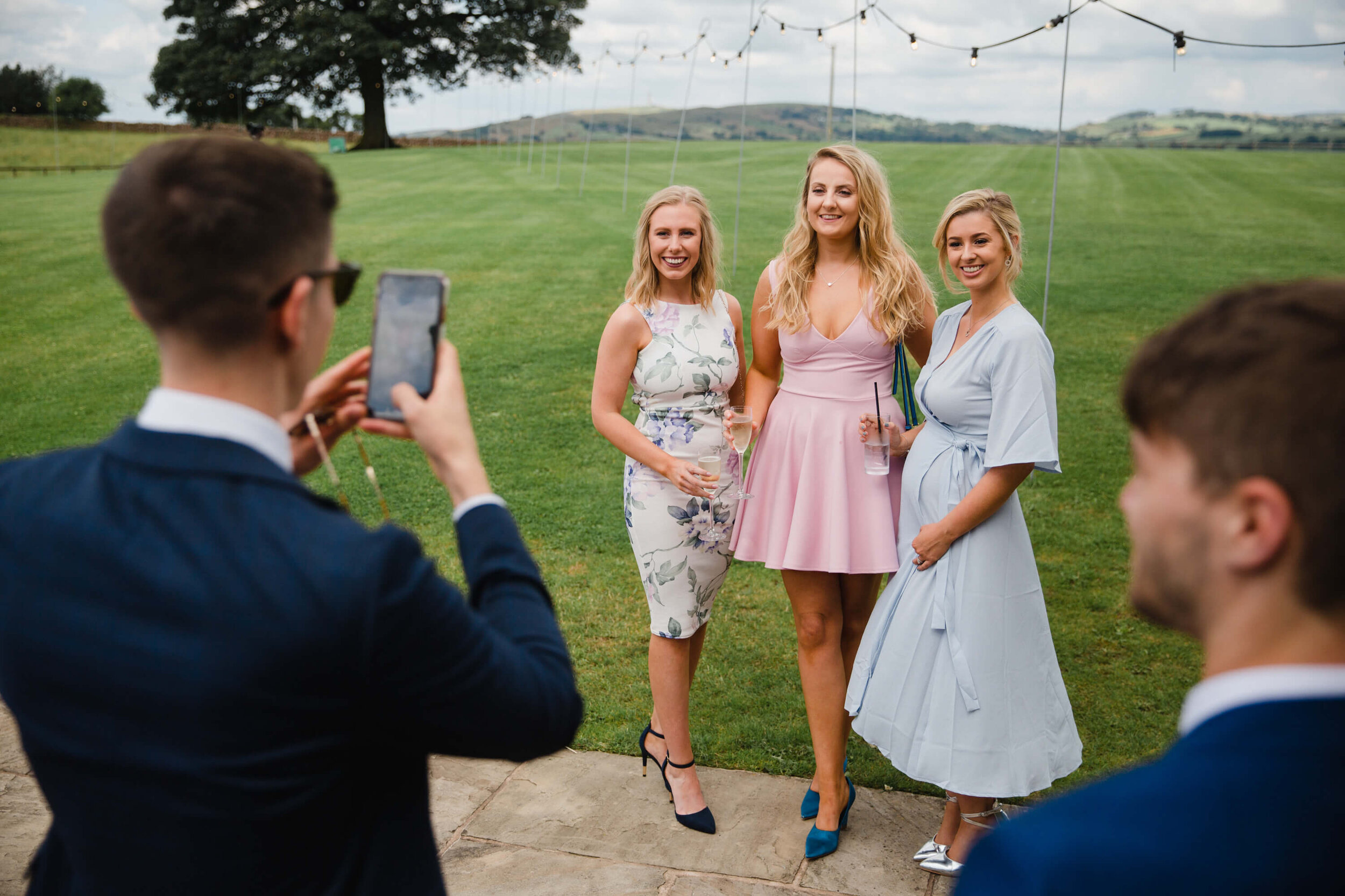 wedding guests have camera phone photograph taken in front of scenic fields
