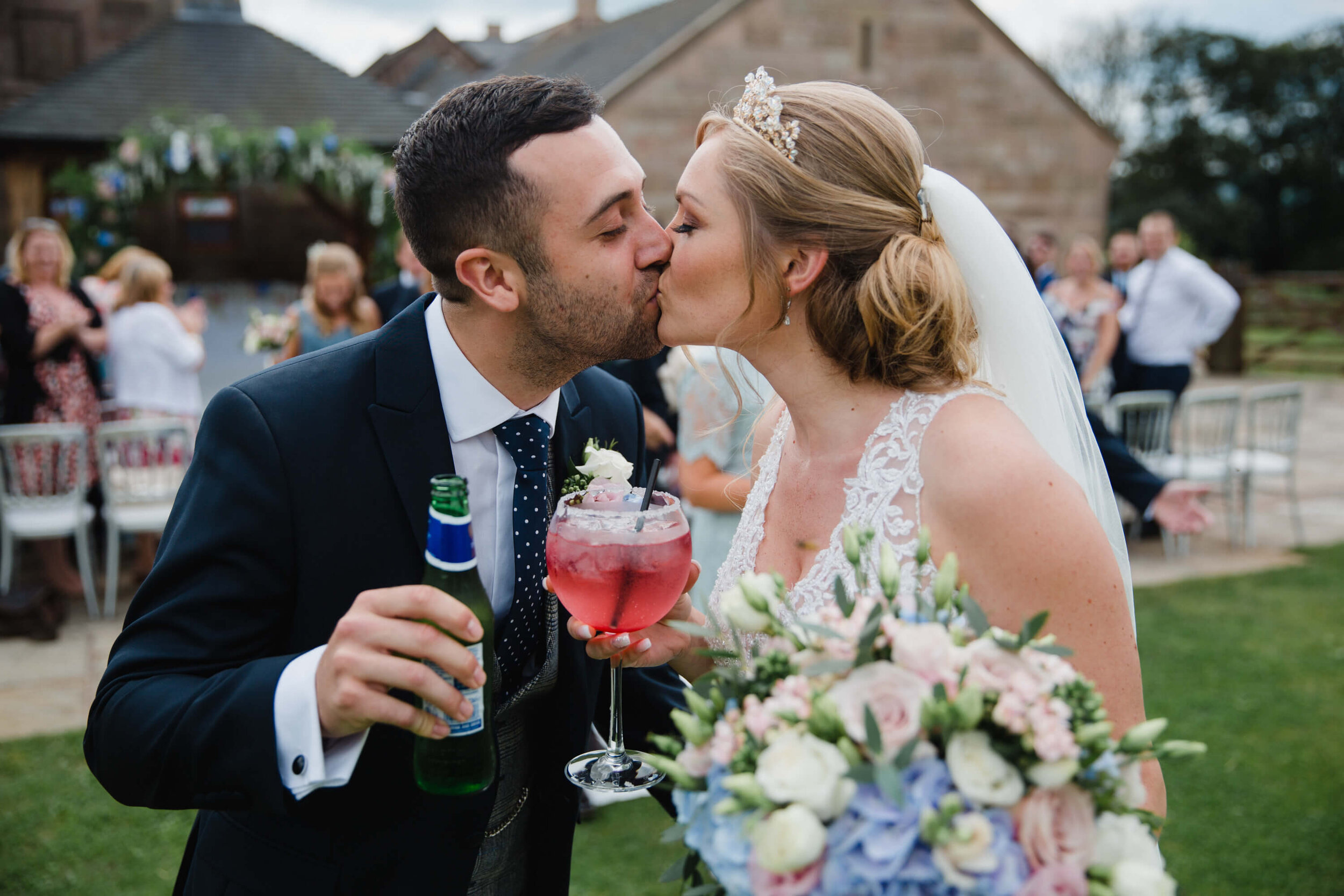 close up kiss of newlyweds holding celebratory drinks