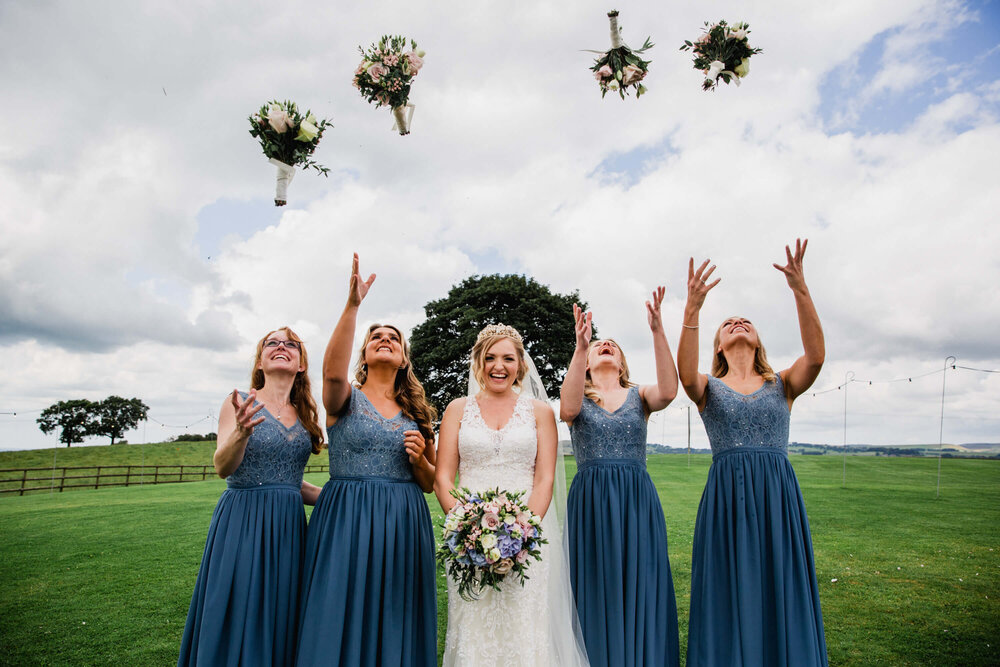 colourful photograph of bridesmaids throwing bouquets in meadow 