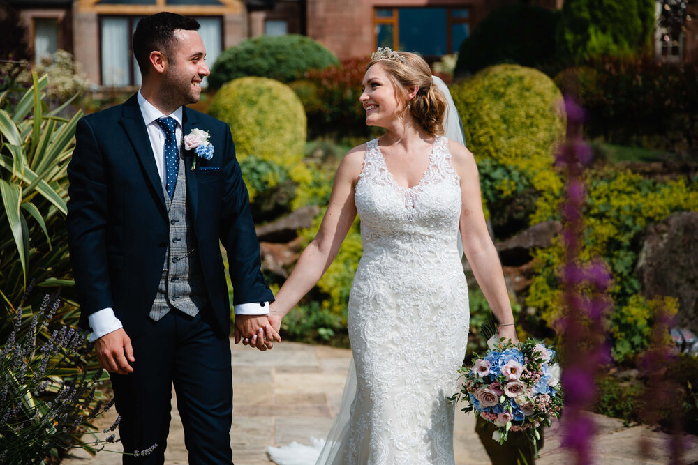 newlyweds hold hands whilst walking in water garden of Heaton House Farm