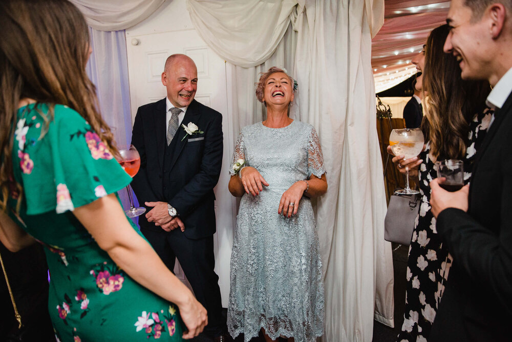 mother of groom laughing at joke while guests enter wedding breakfast room