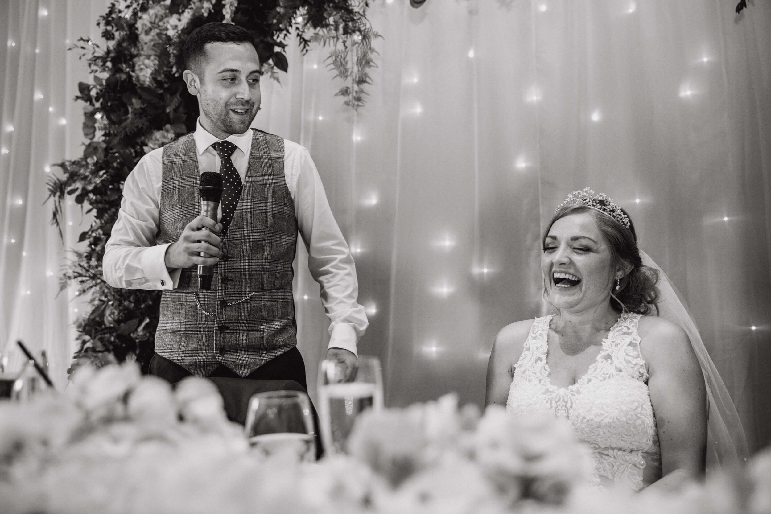 black and white photograph of bride laughing at groom speech