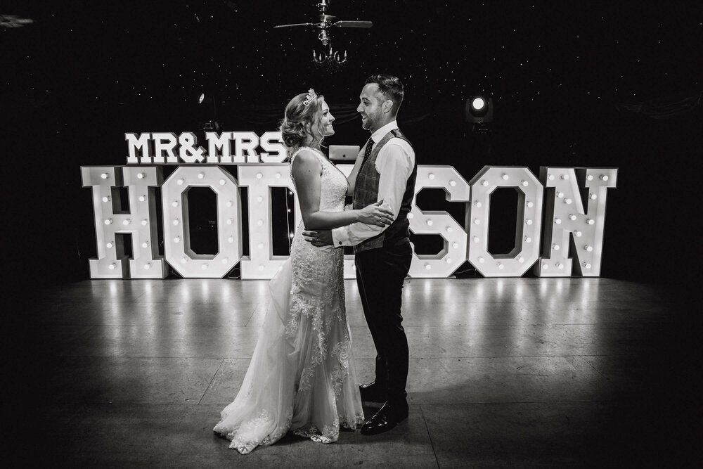 black and white portrait of wedding couple in front of light up lettering