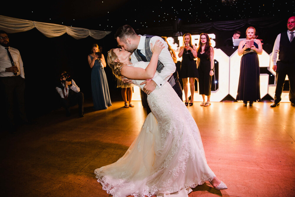 first dance photograph in barn as groom dips bride on dancefloor