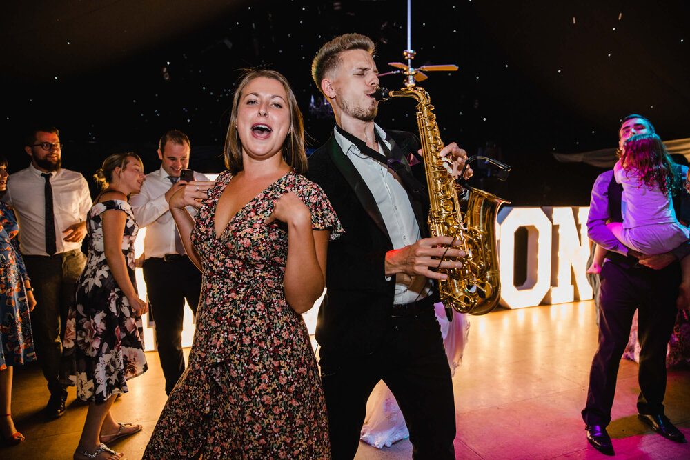 natural moment captured as wedding guest dances with saxophone player