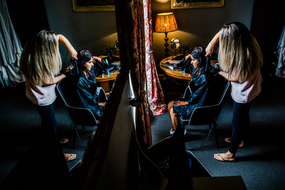 wide angle lens photograph of bride having hair dressed in mirror
