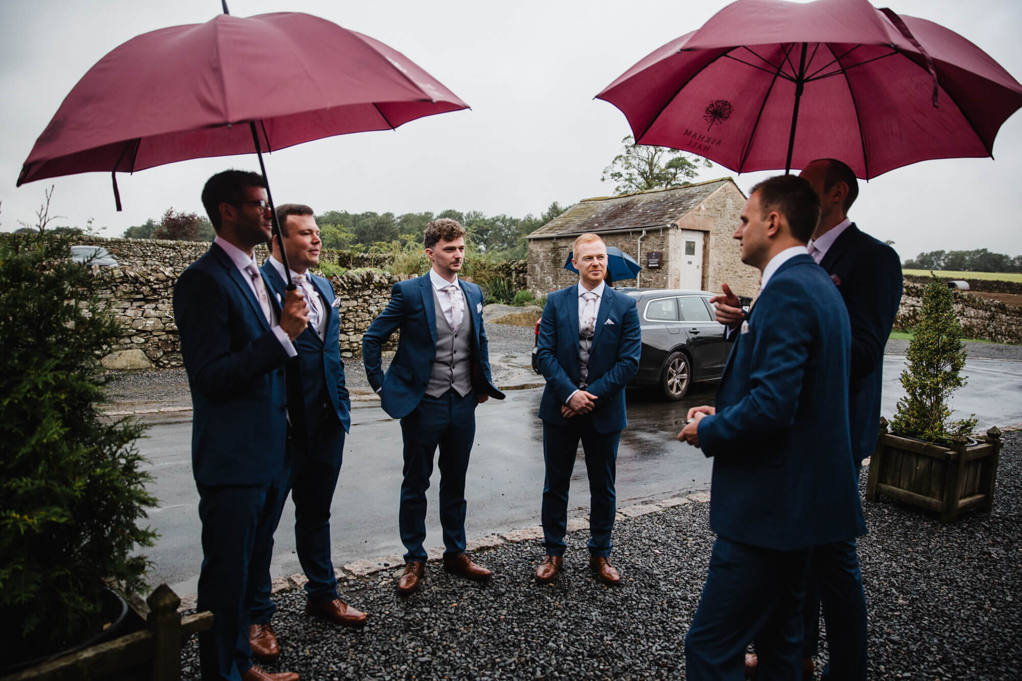 groomsmen group holding umbrellas outside the barn