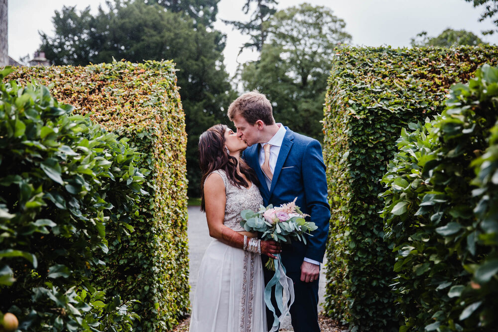 garden portrait as bride and groom kiss by hedges