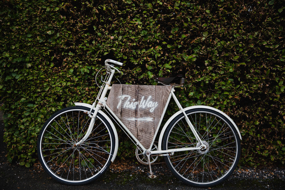 white bicycle rested against hedge with sign to wedding