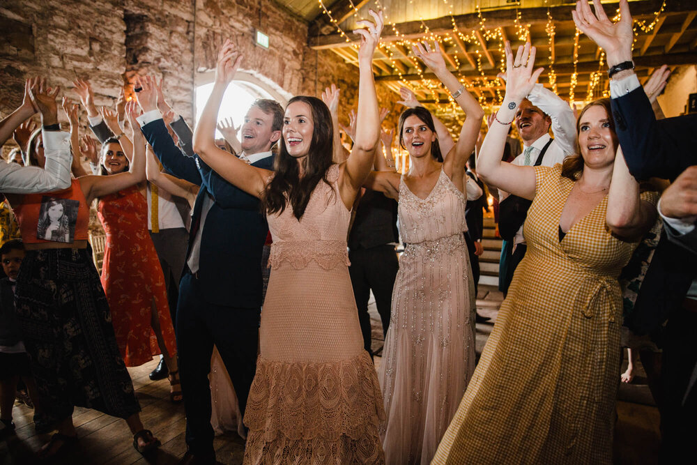wedding party dancing with arms in the air in Askham Hall barn