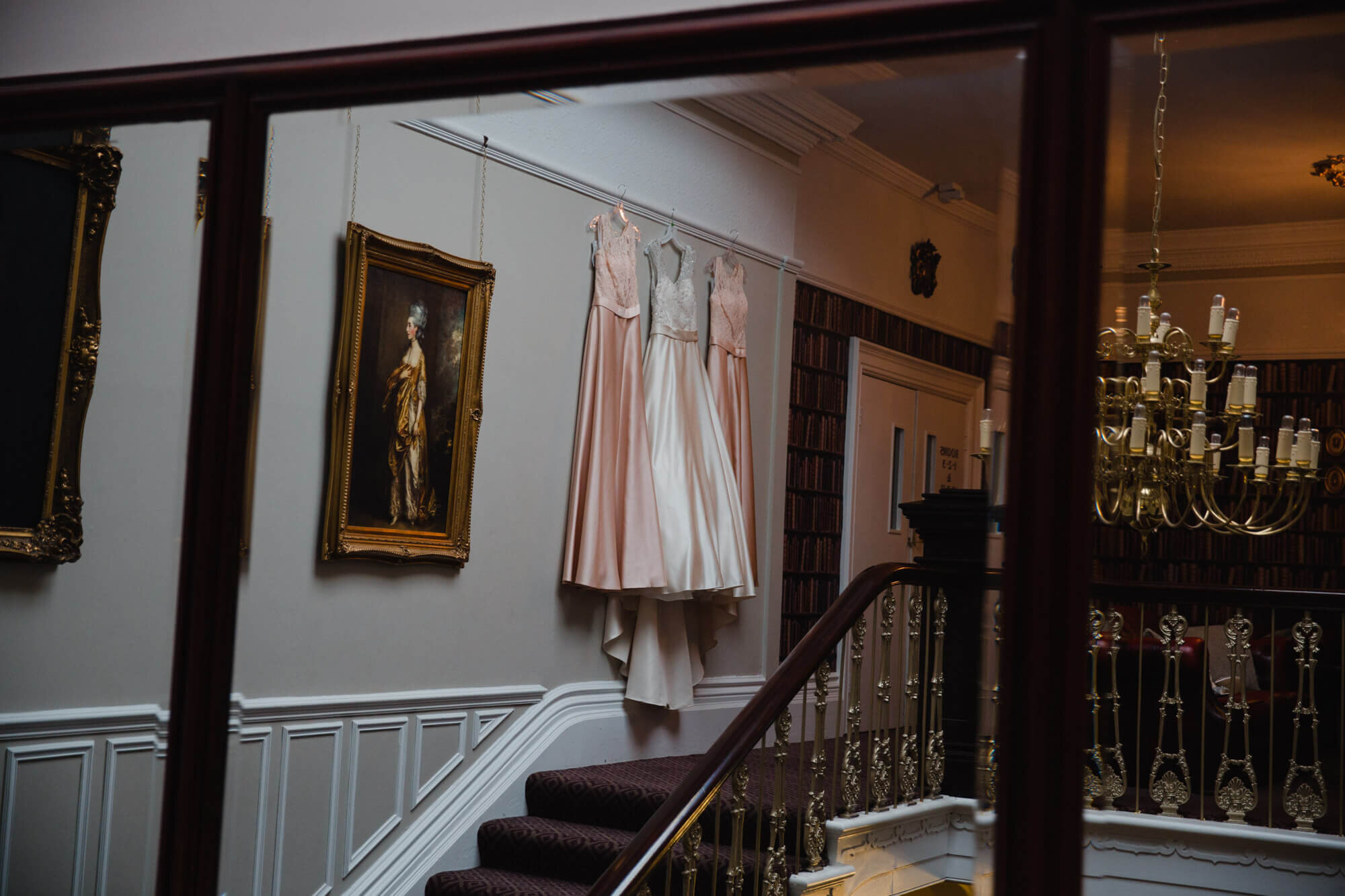 Photograph taken in mirror reflection of wedding dresses hung on staircase wall