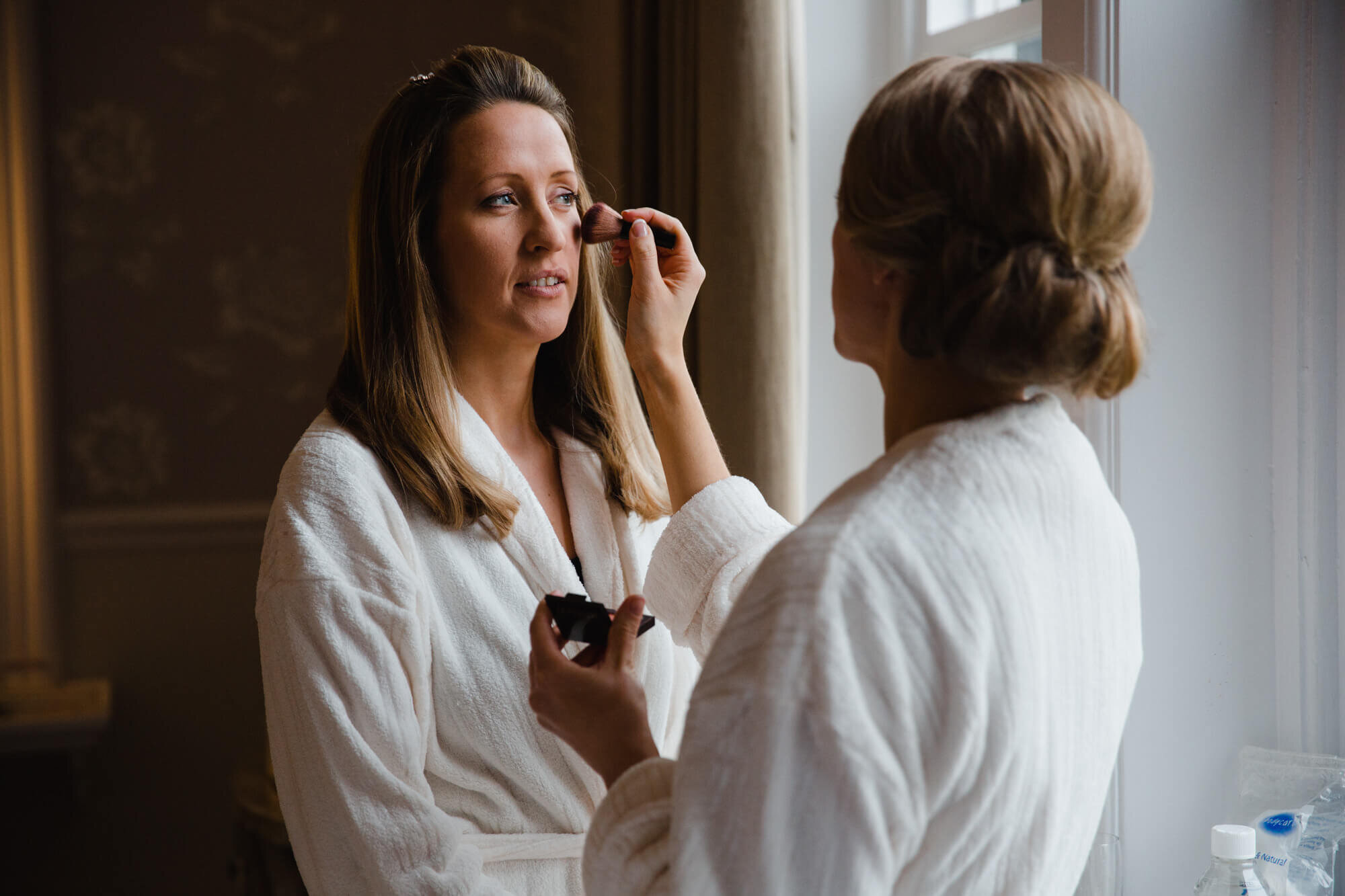 bride adding blusher make up in window light