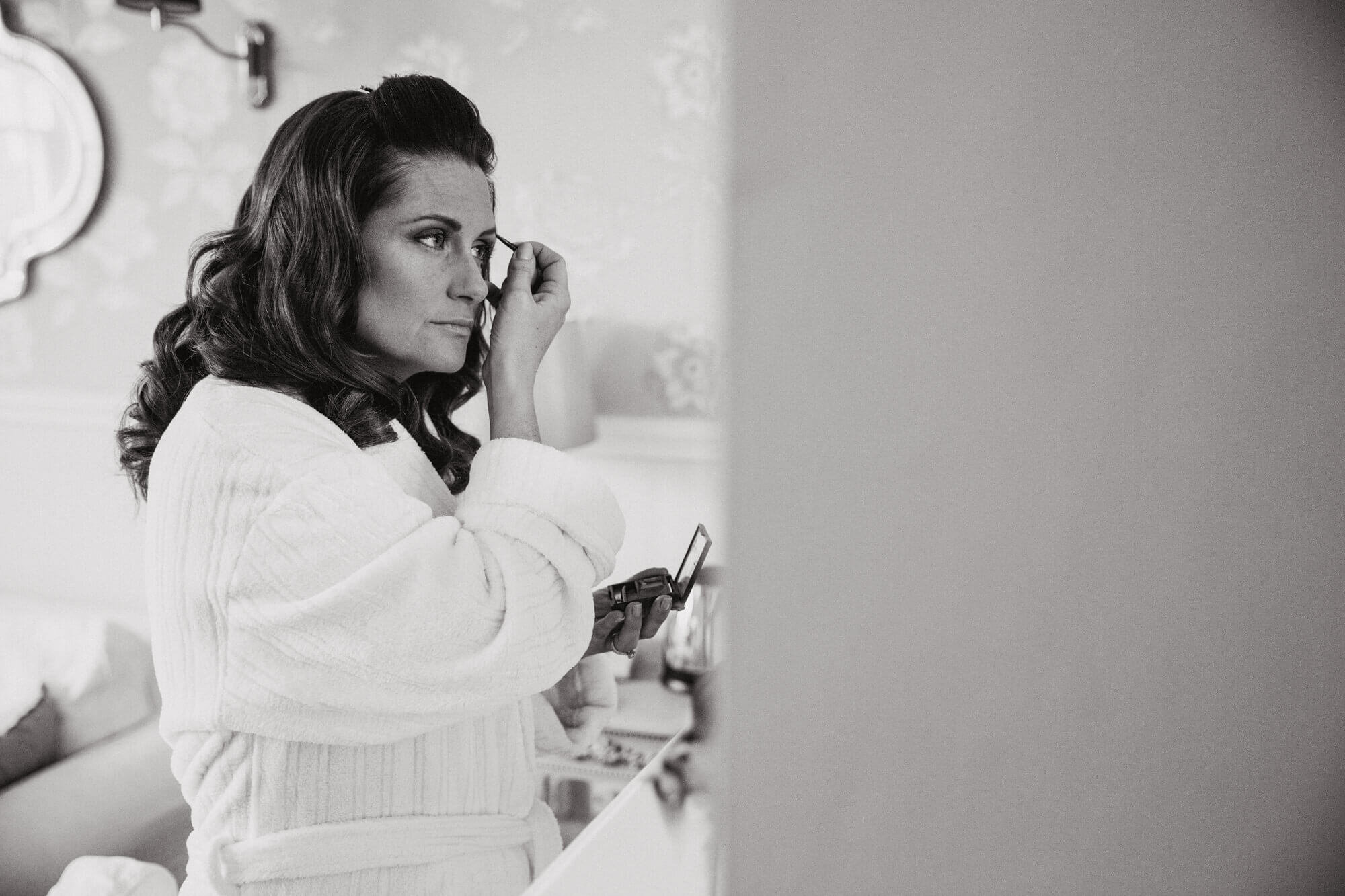 black and white photograph of bridesmaid applying mascara in mirror