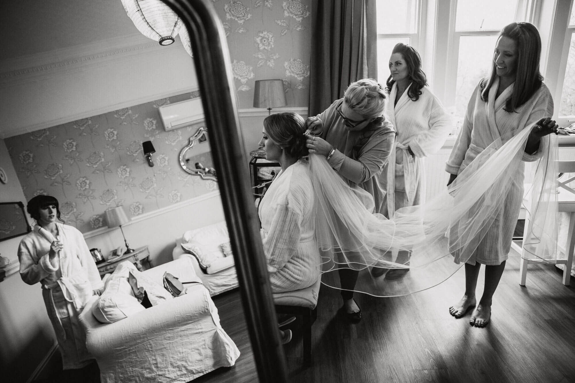 black and white capture of bride having veil fixed to hair with bridesmaids assisting