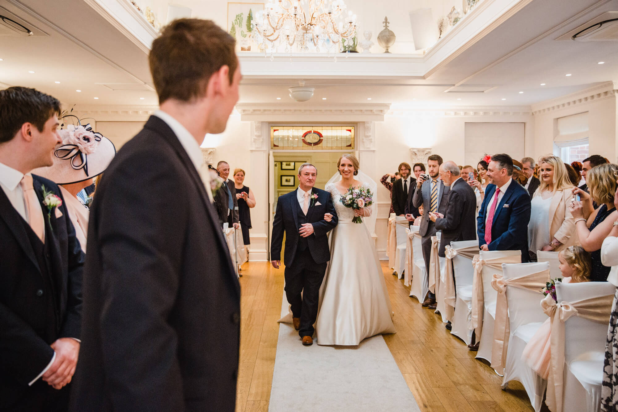 bride and father walking down aisle with groom in foreground