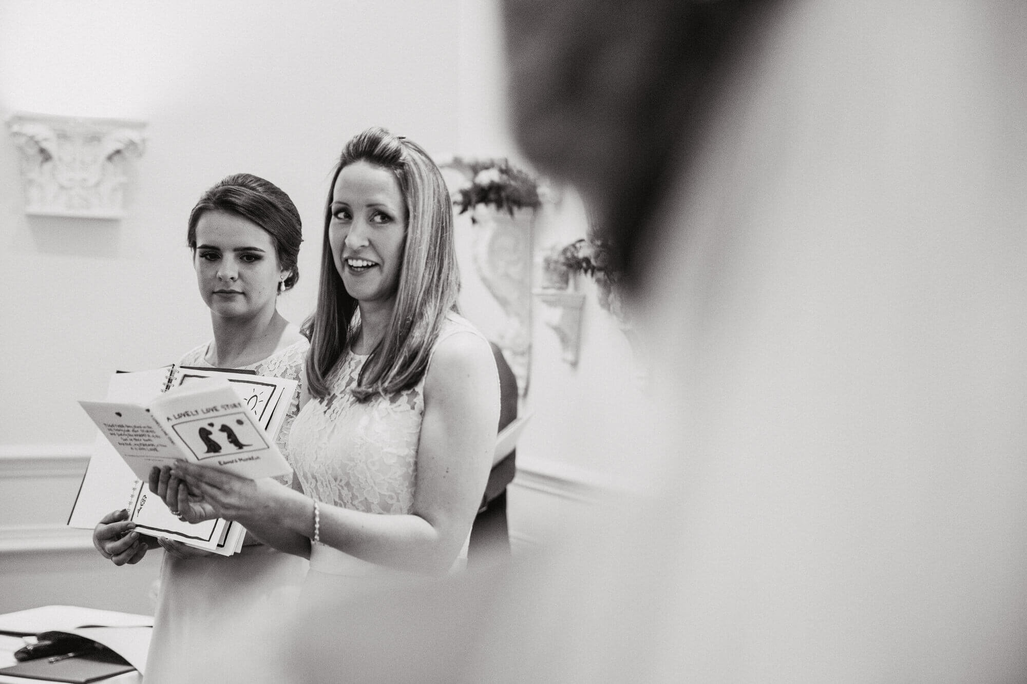 black and white monochrome photography of bridesmaids 'Lovely Love Story' dinosaur book during nuptial service