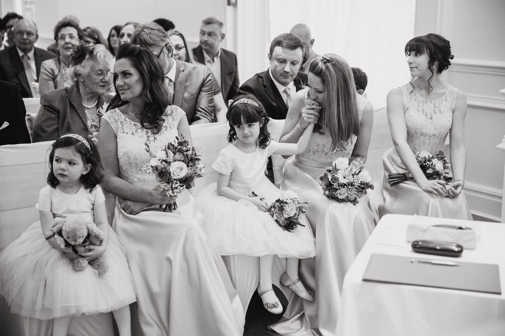 black and white candid moment of bridesmaid kissing hand of flower girl