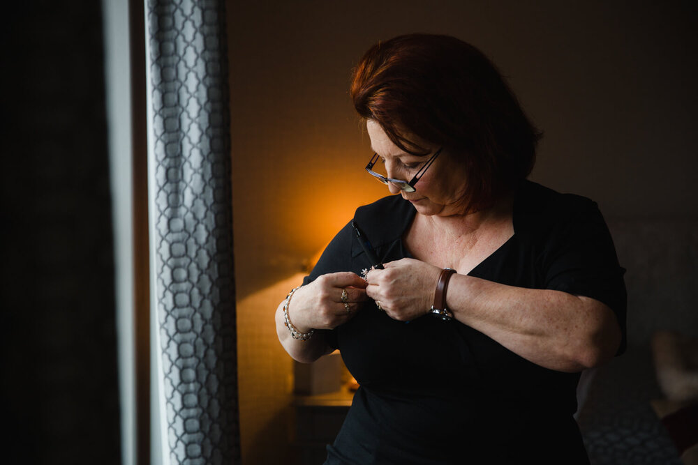 mother pins pinhole floral bouquet to her dress in windowlight