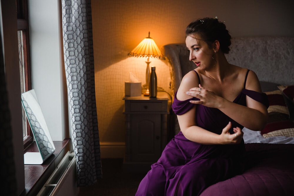 bridesmaid adjusts dress strap in window of preparation room