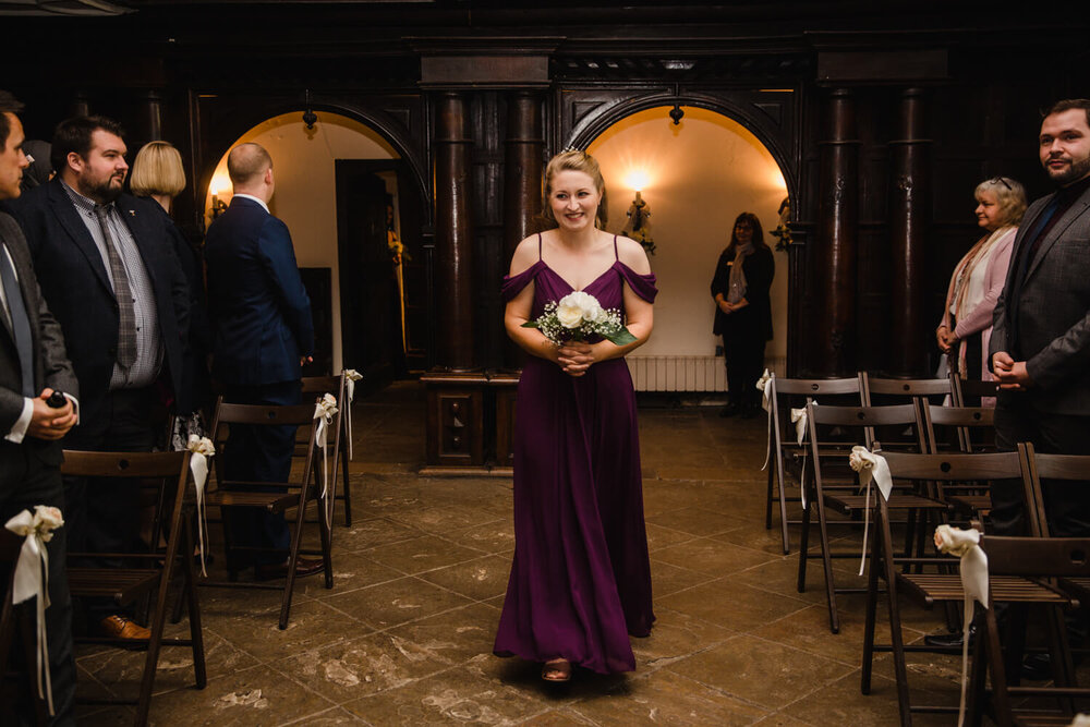 bridesmaid walks down aisle holding bouquet