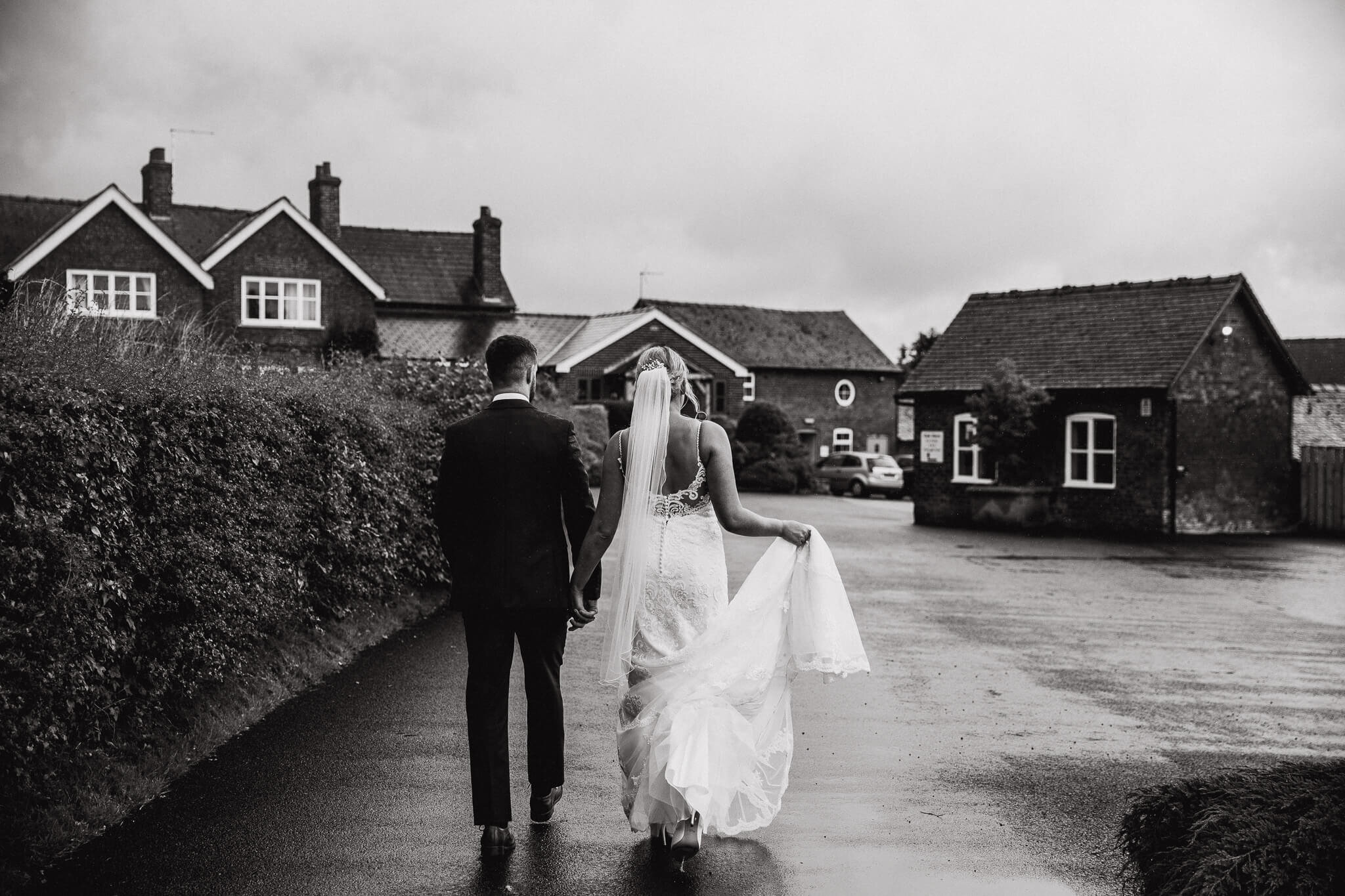 monochrome photograph of bride and groom walking to accommodation 