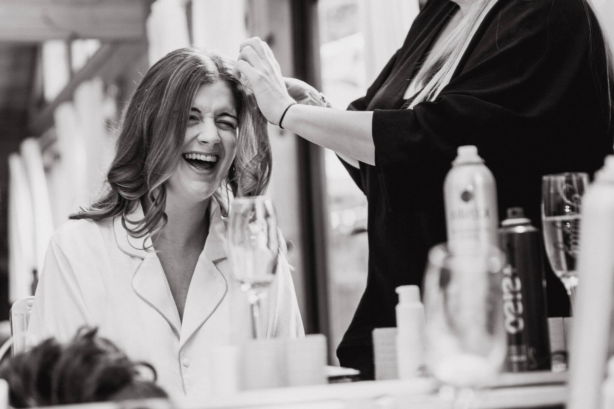 monochrome photograph of bride laughing in the mirror having her hair done