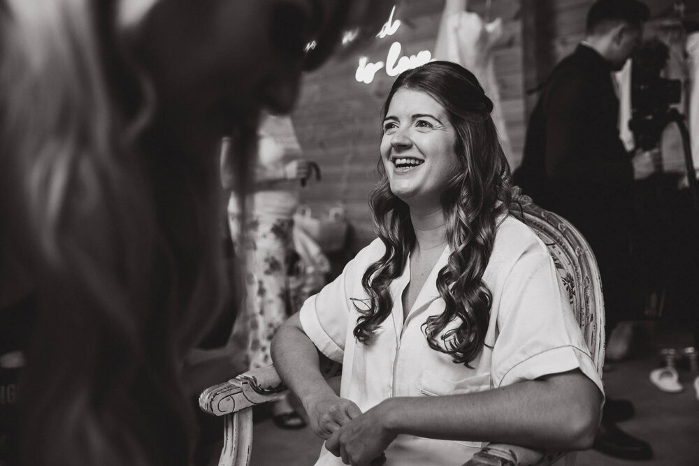 black and white photograph of bride laughing during make up