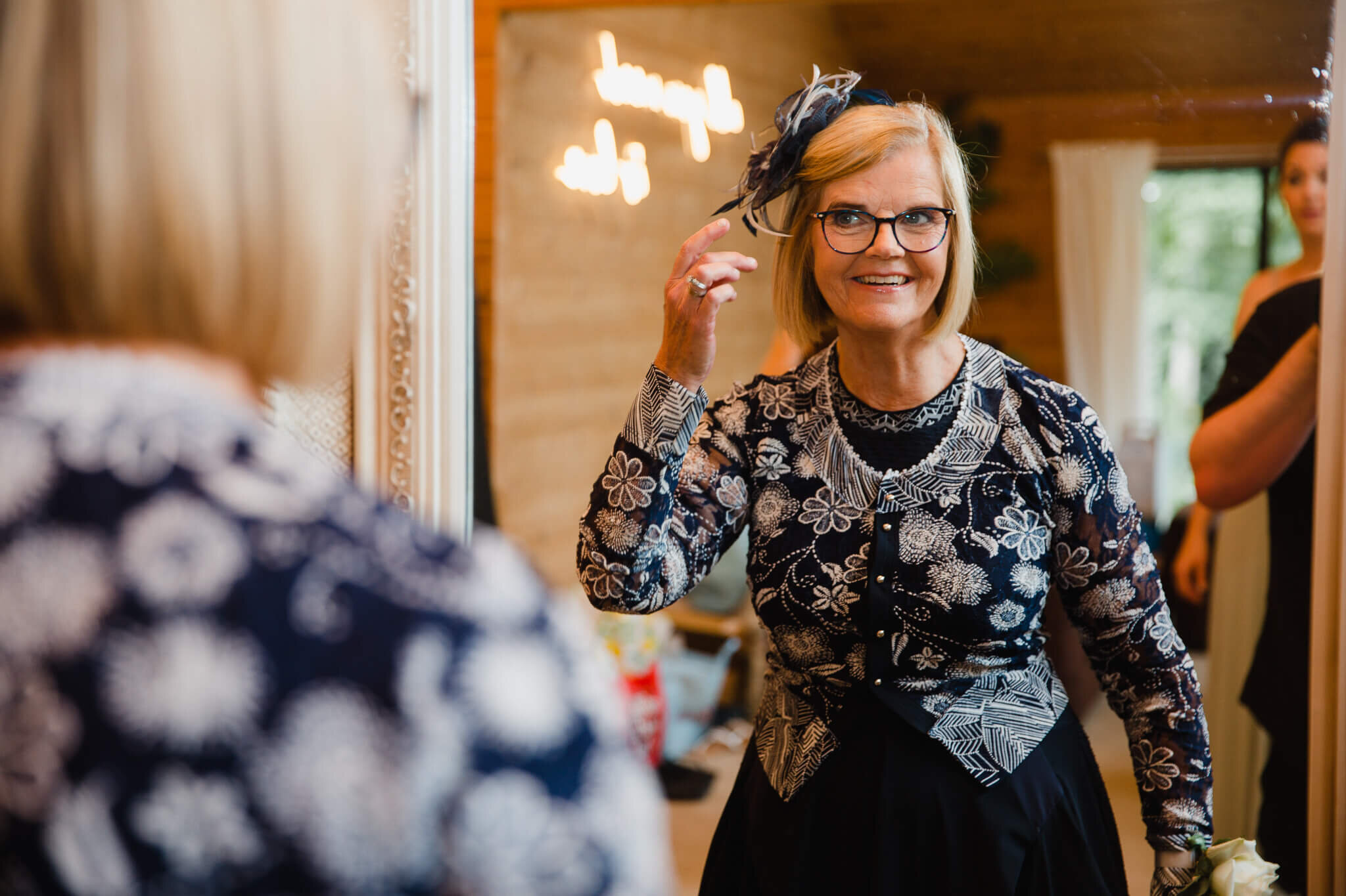 mother of bride fixing fascinator while smiling in mirror