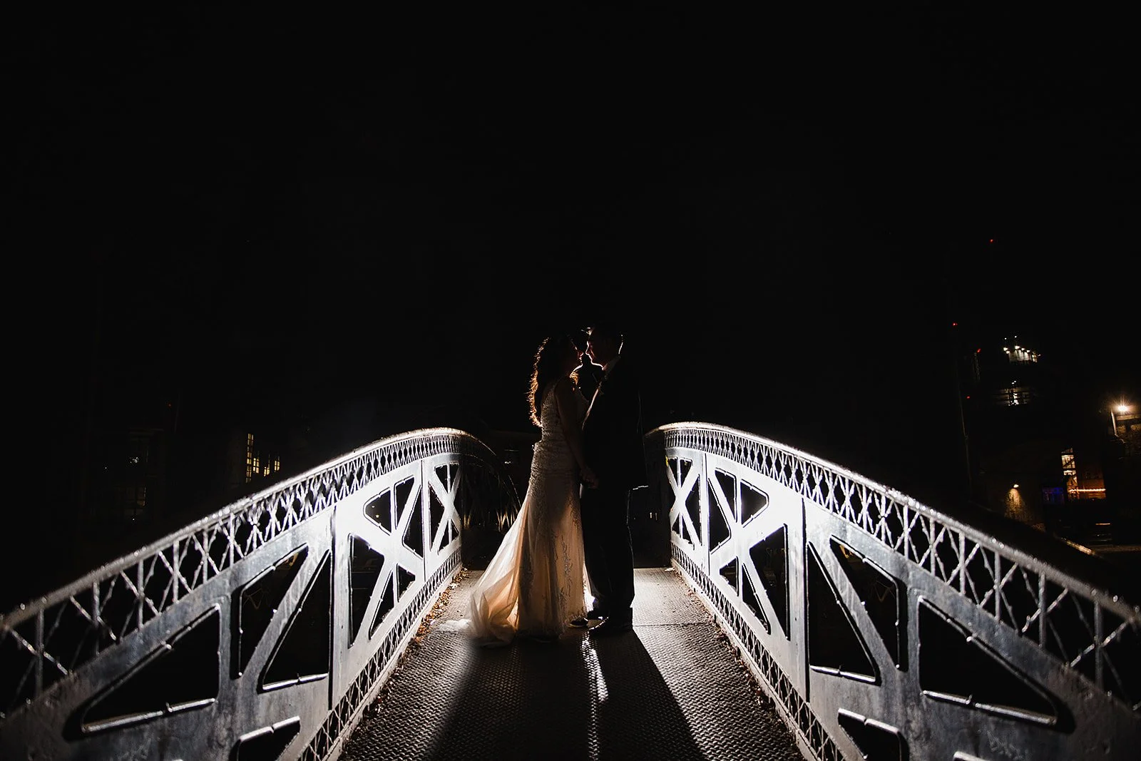 Bride and groom silhouetted on illuminated canal bridge at The Castlefield Rooms wedding venue in Manchester at night