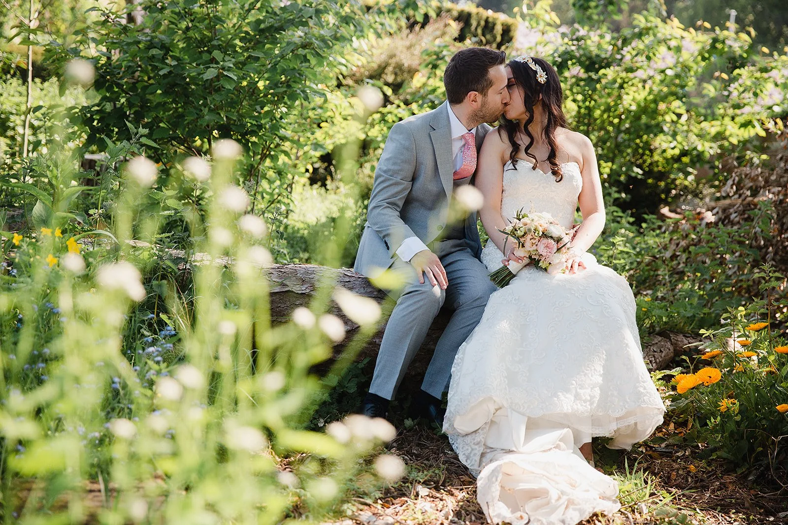 Bride and groom sitting together on a fallen tree in Inglewood Manor’s gardens, surrounded by greenery and soft spring light.