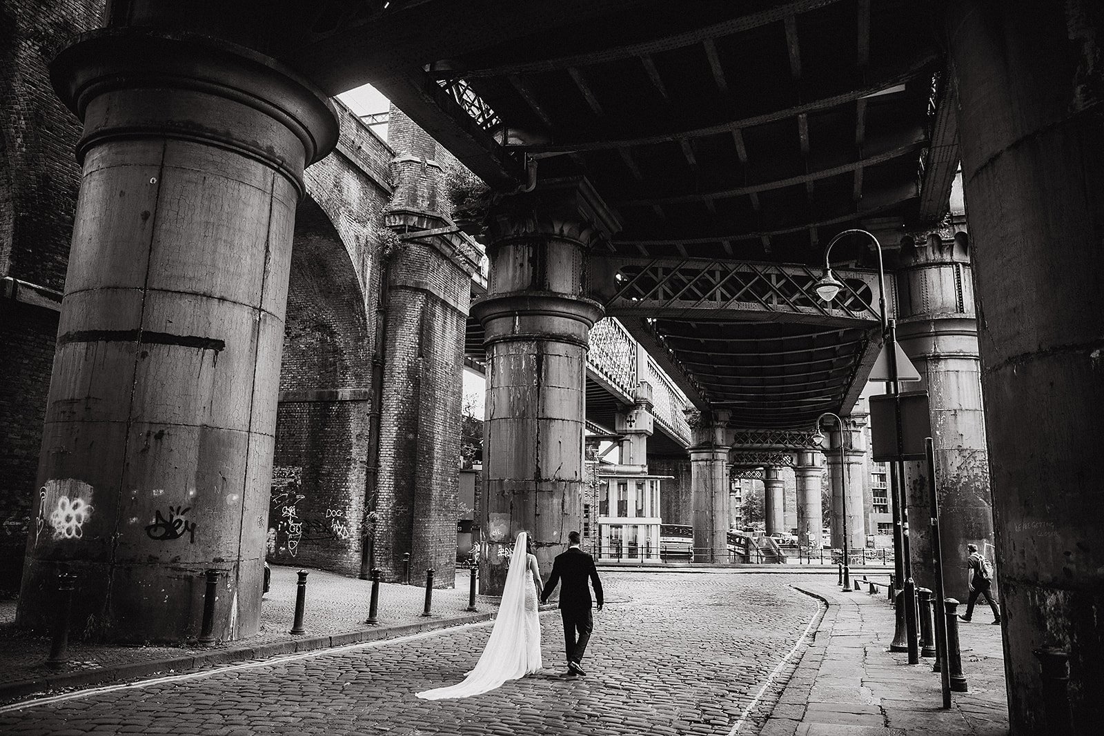 Bride and groom walking beneath the railway bridges and industrial viaducts in Castlefield Manchester during a wedding at The Castlefield Rooms.