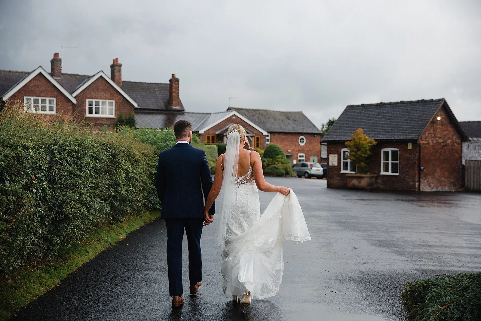 Bride and groom walking across wet driveway at Sandhole Oak Barn wedding venue in Cheshire after rain