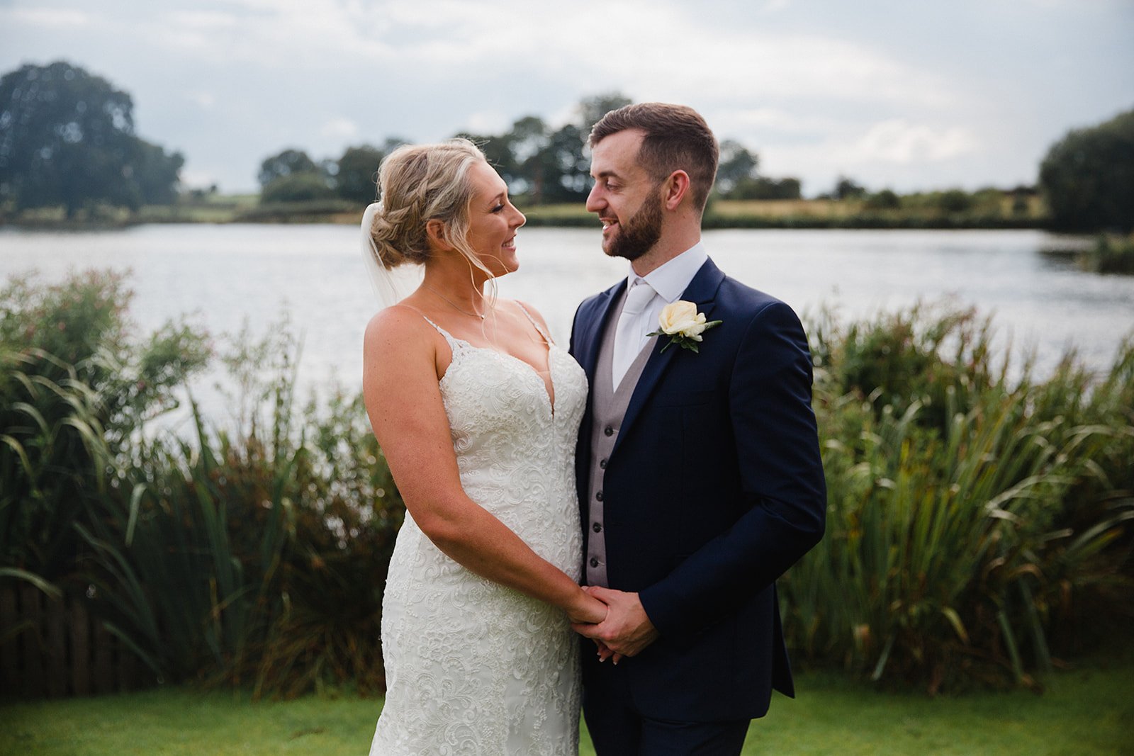 Bride and groom standing by the lake at Sandhole Oak Barn during their summer wedding, captured in a relaxed documentary style.