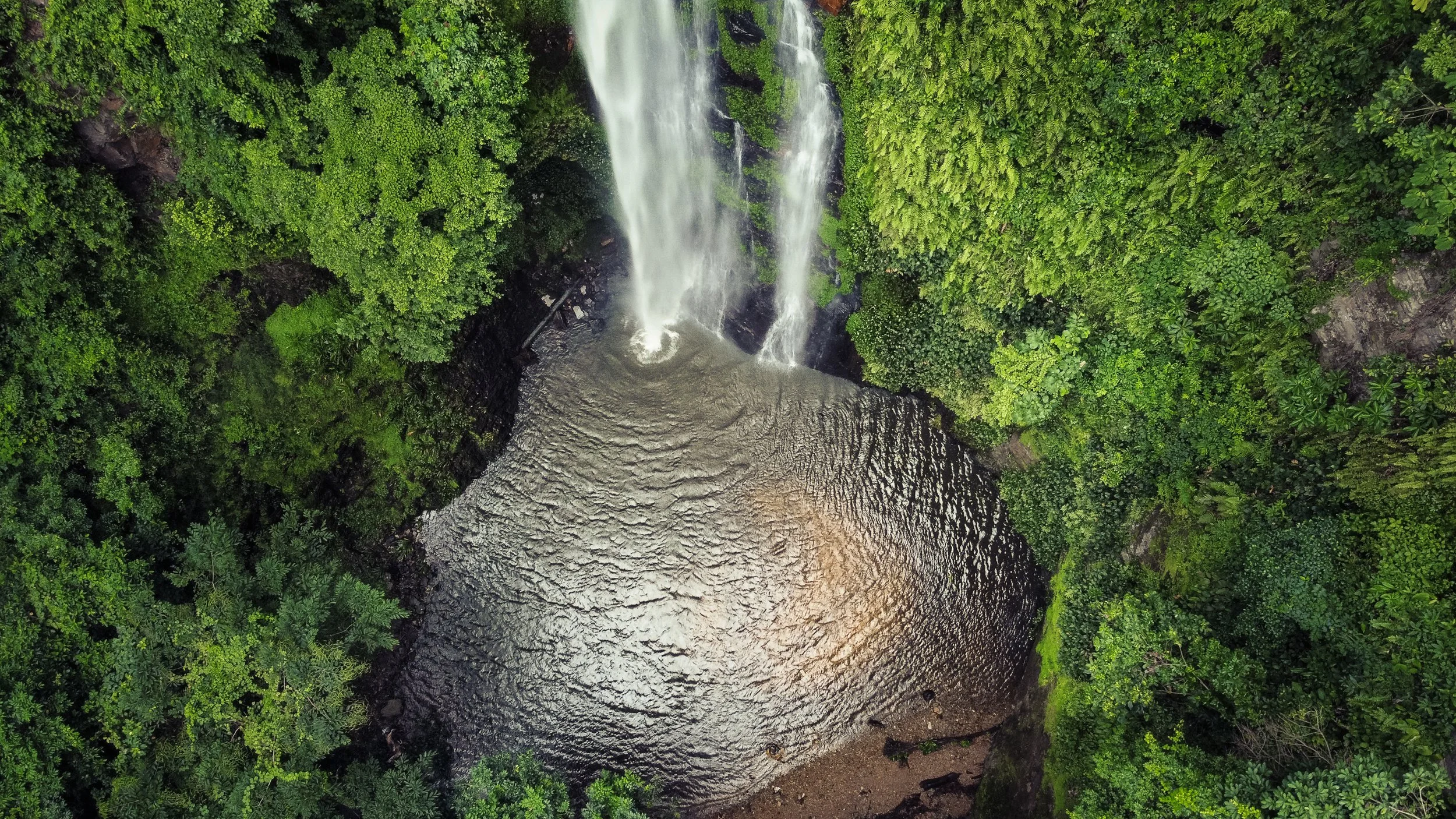 An aerial image of Tagbo Waterfall cascading into a pool below and surrounded by steep, lush canopy