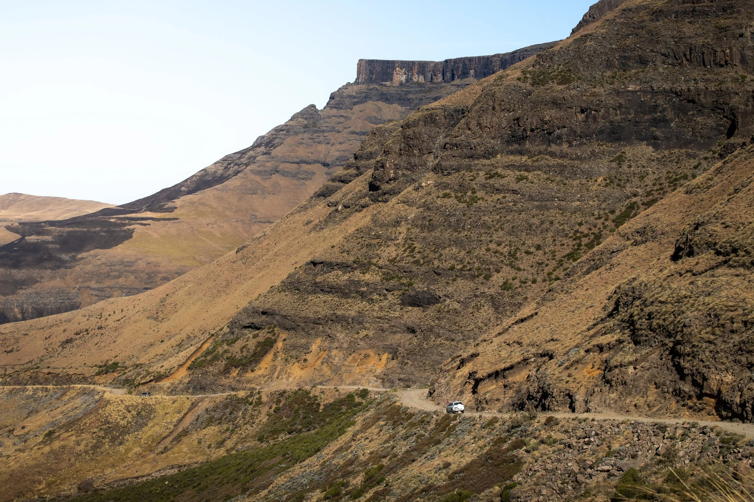 A white car carefully navigates the winding road of the Sani Pass, descending from Lesotho into South Africa