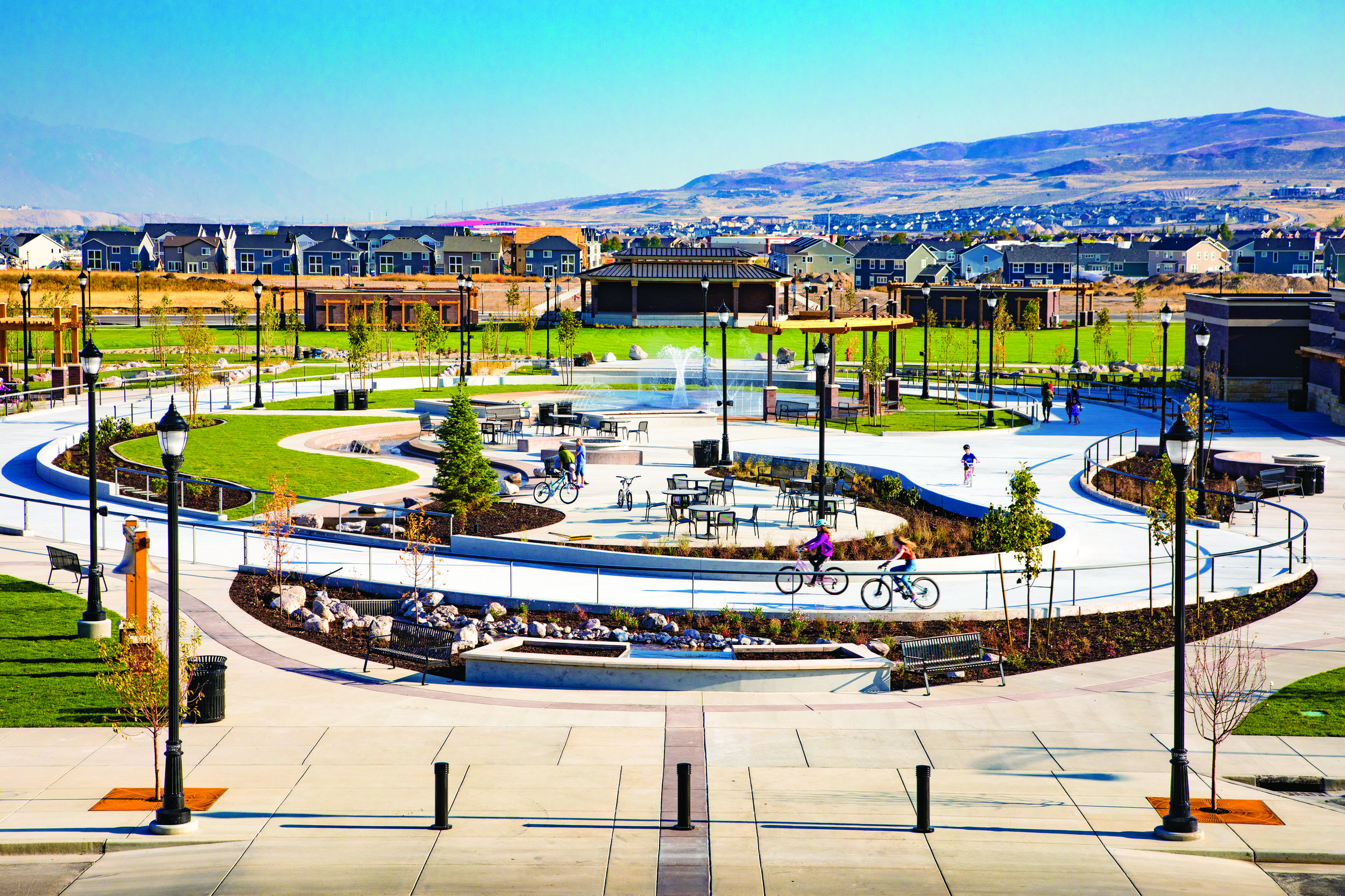  Looking toward the bandstand across J Lynn Crane Park from the steps of City Hall, many of the significant elements of the Towne Center are visible. The Ice Ribbon, being used by cyclists in this photo, surrounds the Splash Pad, Interactive River, F