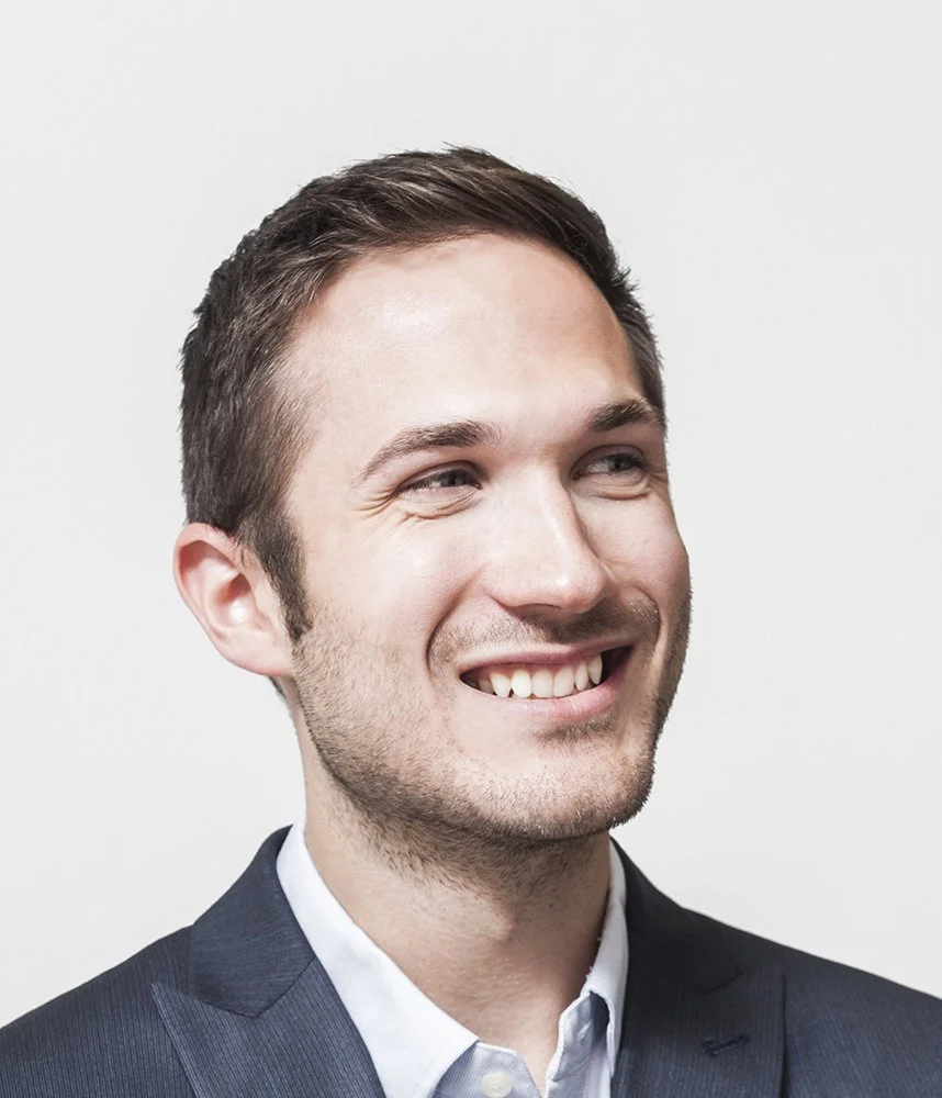 Peter smiling in a suit, looking to the side, against a plain background.