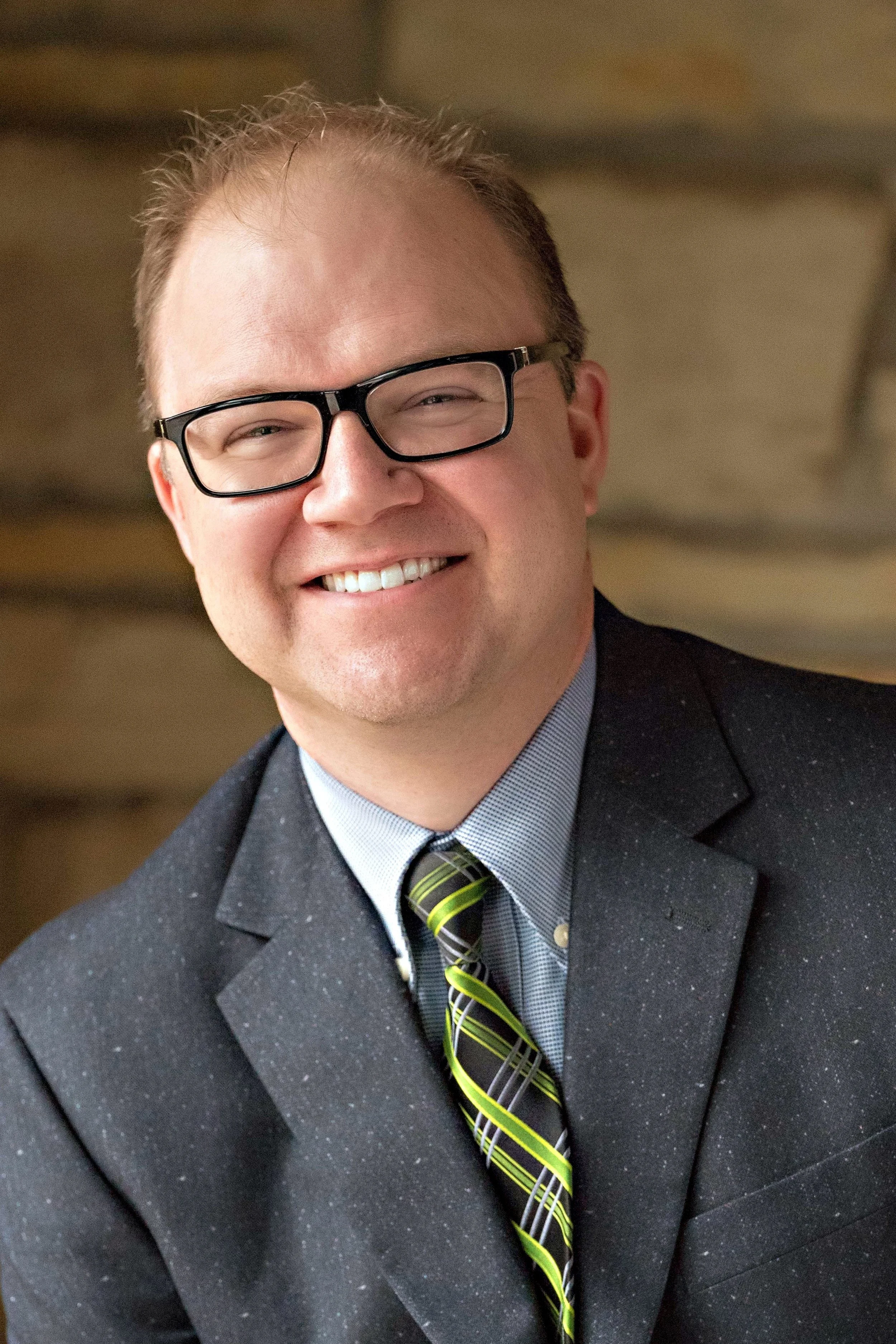 Aaron smiling wearing glasses, a suit, and a green striped tie.