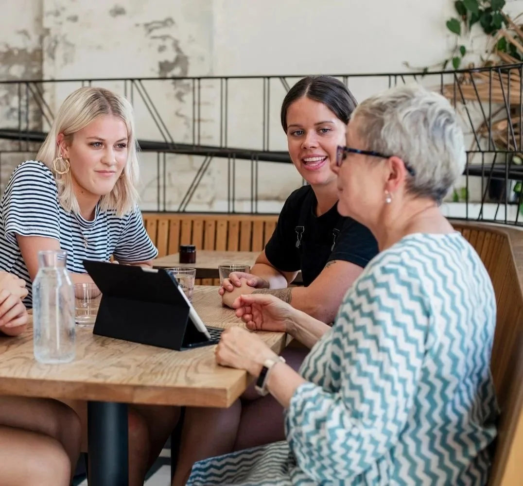Three women of different ages around a table, looking at a tablet