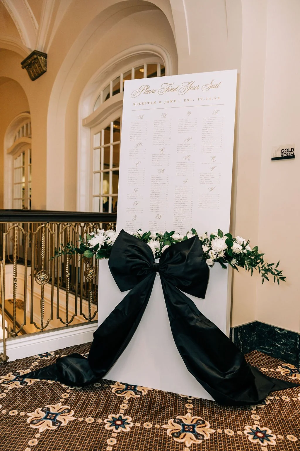 Wedding seating chart with floral decoration and large black bow in an elegant setting.