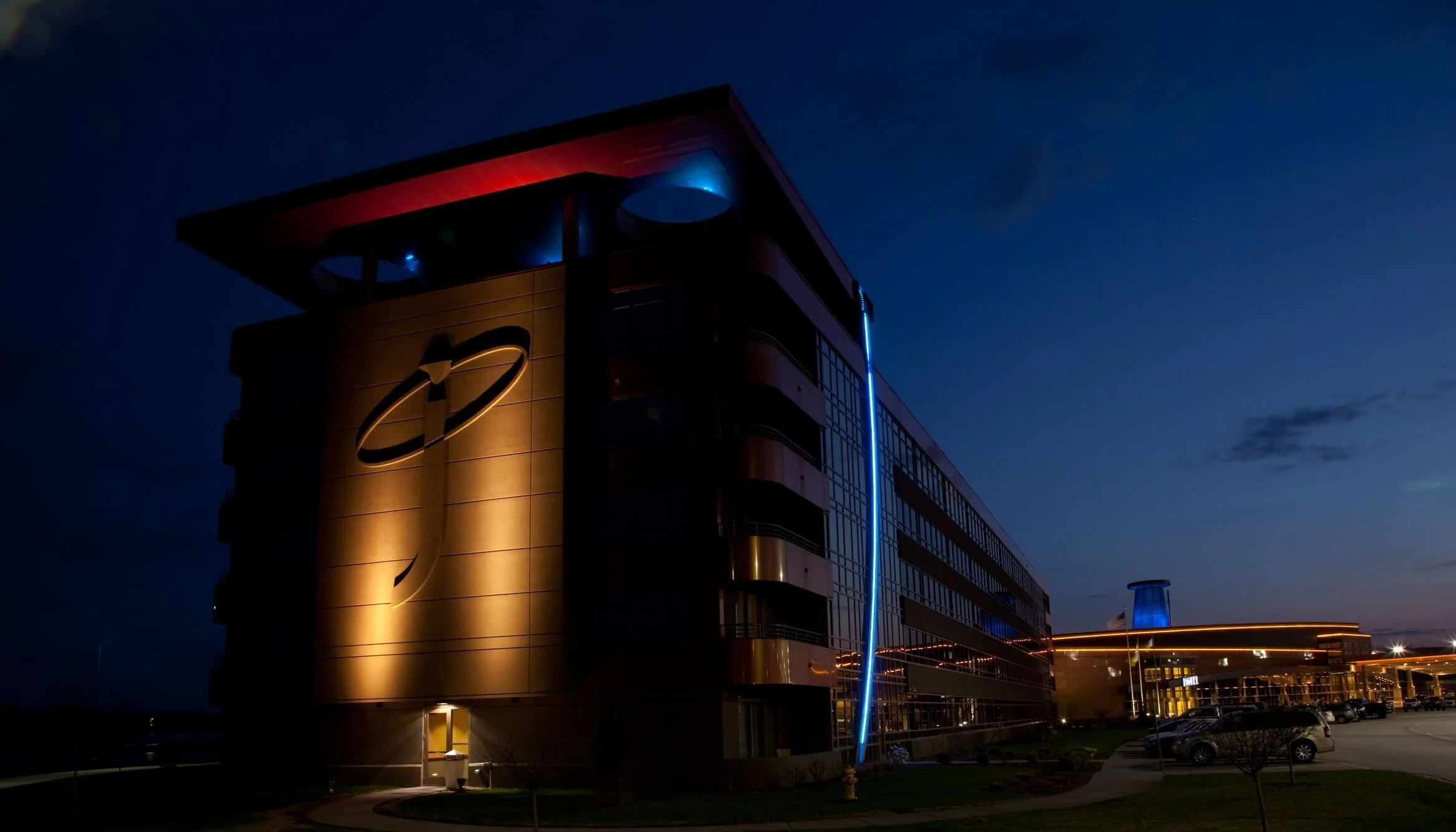 Exterior of a modern building with illuminated signage at dusk, featuring a curved, sleek design and glowing lights.